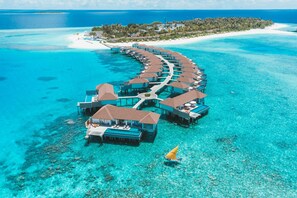 An overwater resort with multiple bungalow-style accommodations connected by walkways, surrounded by clear turquoise waters and a distant island. - Avani+ Fares Maldives Resort (Fares)