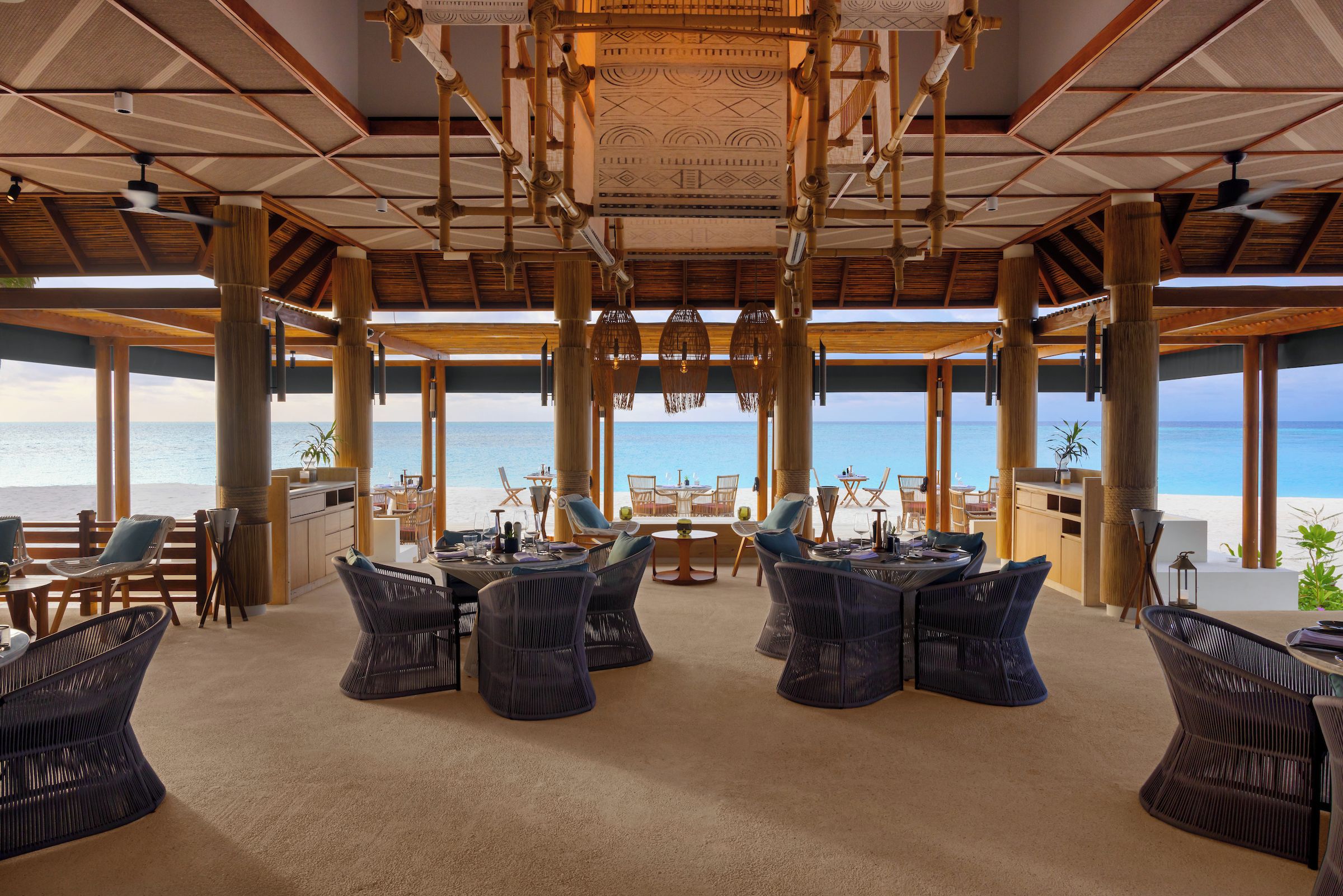 A beachside lounge with wicker furniture, large windows, and a view of the ocean.