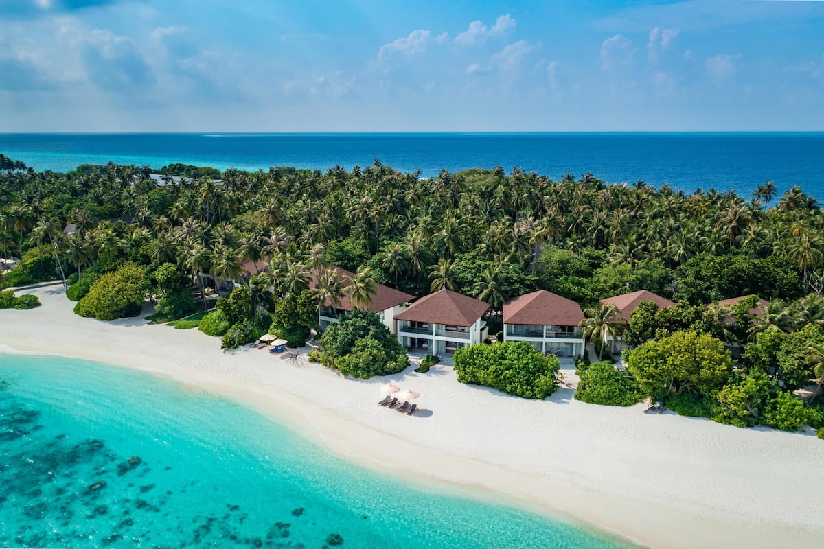 An aerial view of a beach resort with overwater bungalows, a white sandy beach, and clear turquoise waters.