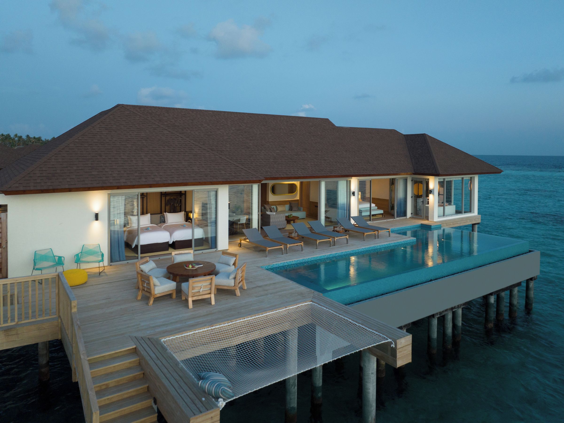 A modern overwater villa with a private infinity pool, multiple bedrooms, and a deck with outdoor seating.