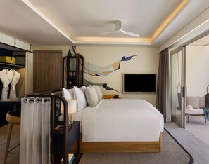 Een hotelkamer met een bed, een bureau, een stoel, een televisie en een plafondventilator.