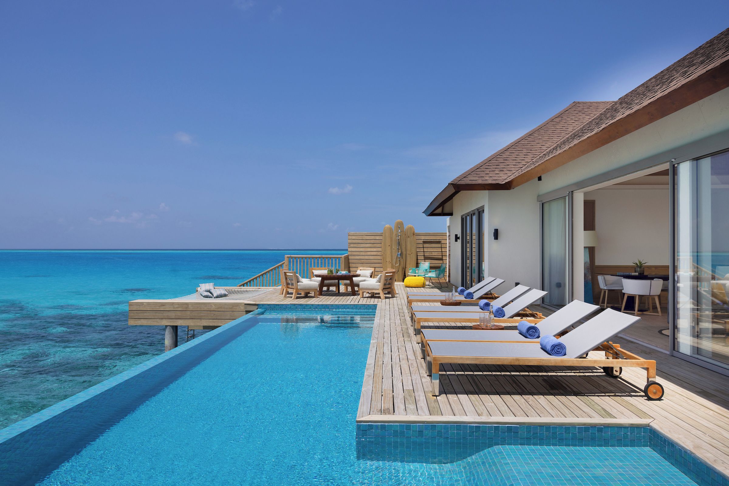 An infinity pool with lounge chairs and a wooden deck overlooking the ocean.