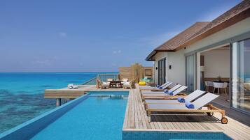 An infinity pool with lounge chairs and a wooden deck overlooking the ocean.