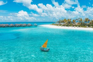 A clear turquoise sea with a sailboat, overwater bungalows, and a beach with palm trees. - Avani+ Fares Maldives Resort (Fares)