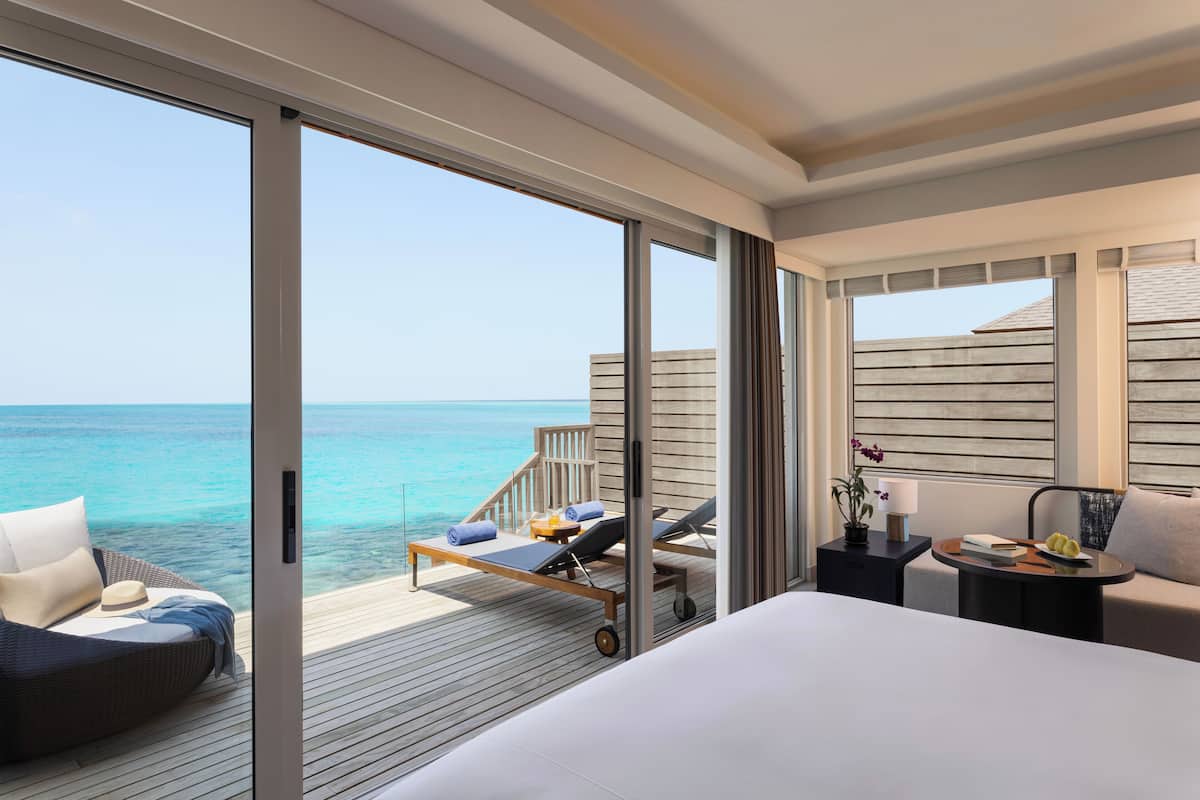 A modern hotel room with a large bed, a sofa, and a balcony with a view of the ocean.