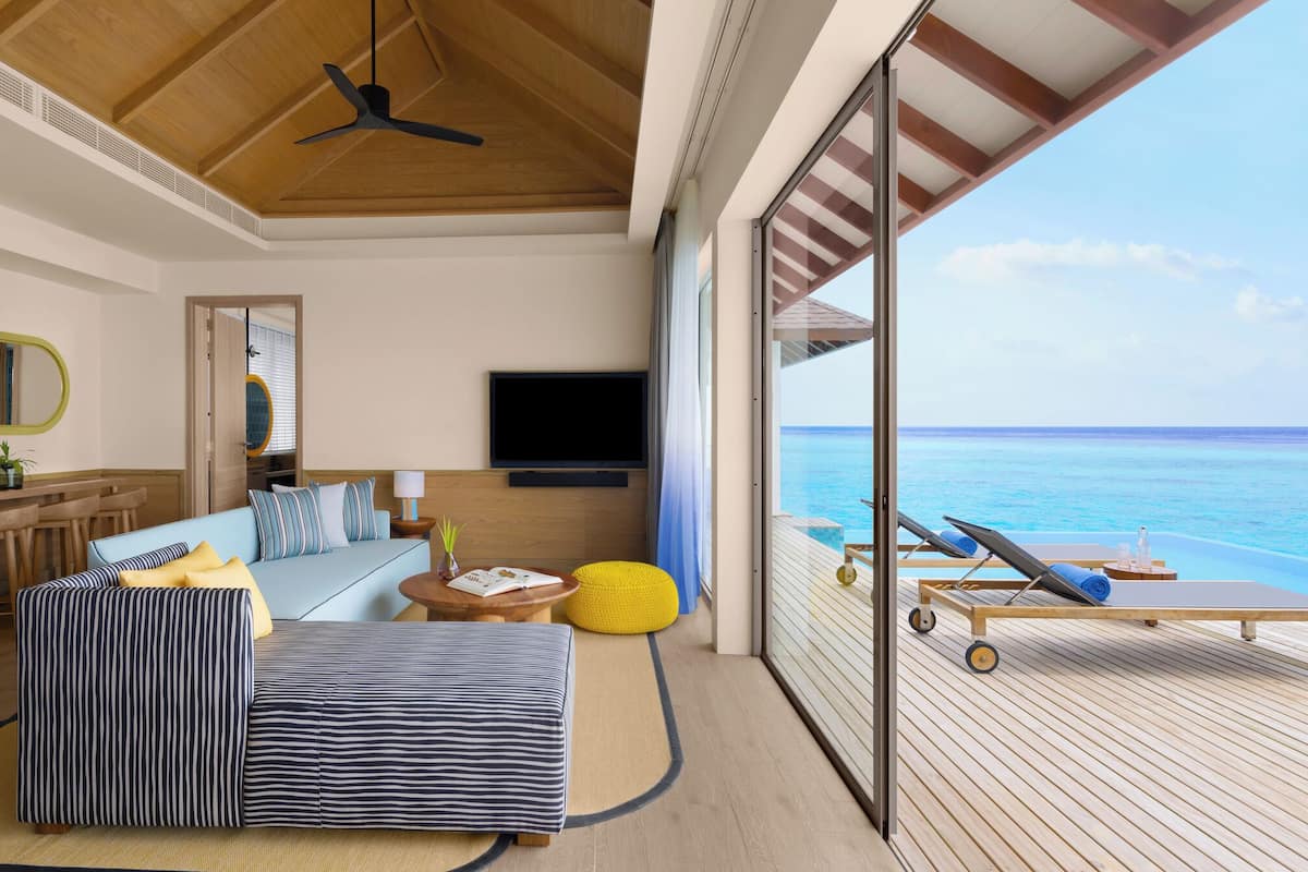 A modern room with a wooden ceiling, a TV, a sofa, a dining table, and a view of the ocean.