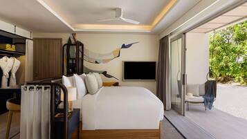 Habitación de hotel moderna con una cama grande, ventilador de techo, televisor y vistas a la playa.