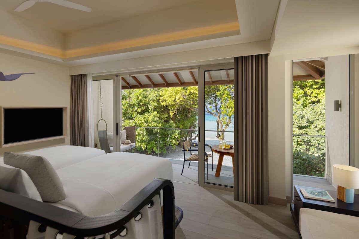 A hotel room with a large bed, a flat-screen TV, a balcony with a table and chairs, and a view of the sea.