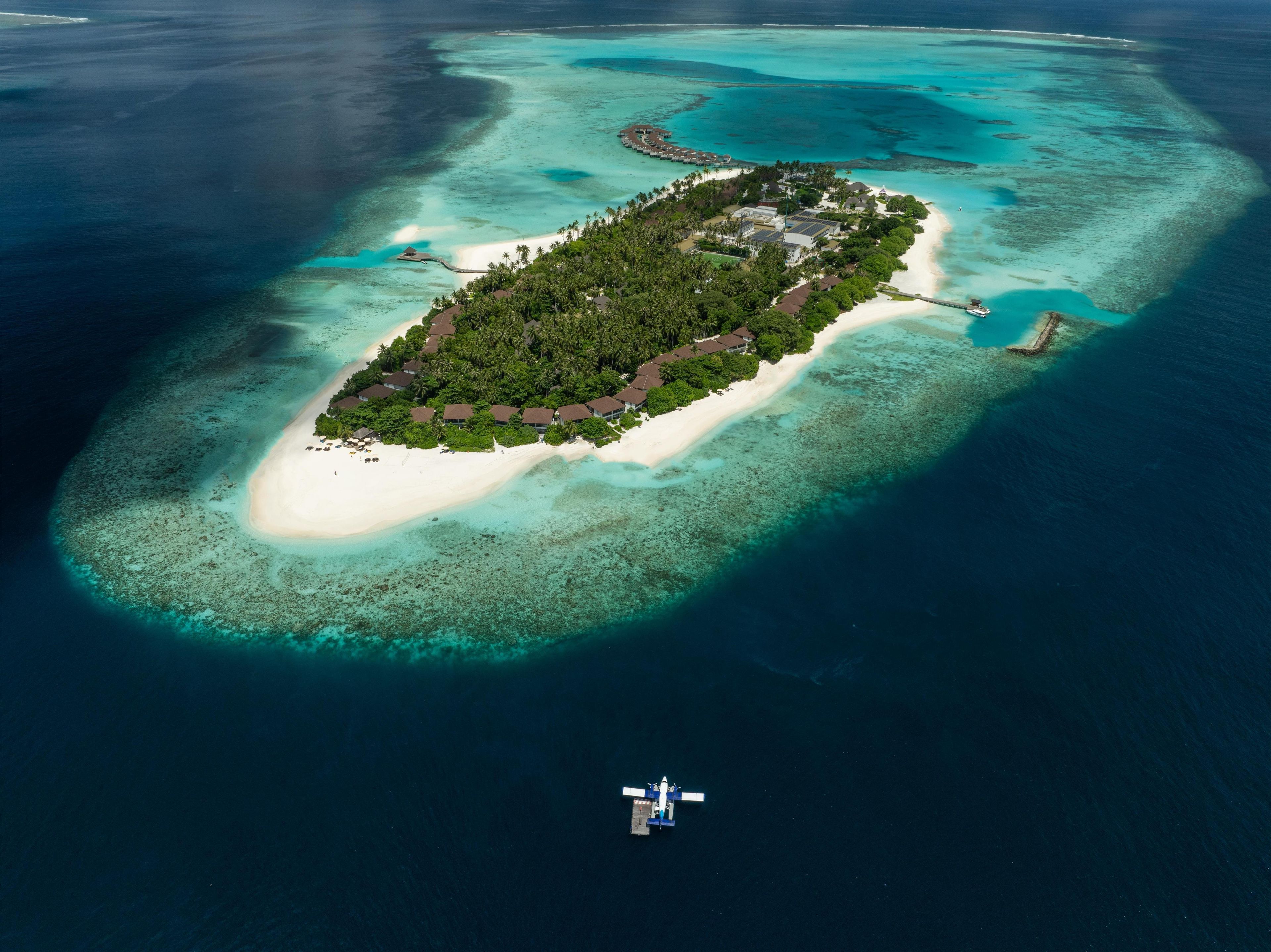 An aerial view of a tropical island with a white sandy beach, dense green vegetation, and clear turquoise waters.