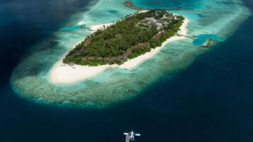 An aerial view of a tropical island with a white sandy beach, dense green vegetation, and clear turquoise waters.