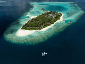 An aerial view of a tropical island with a white sandy beach, dense green vegetation, and clear turquoise waters.