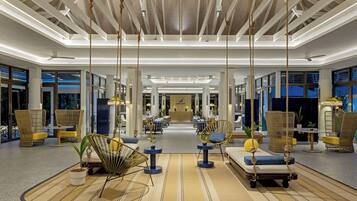 A modern hotel lobby with hanging ropes, wicker furniture, and a central reception desk.