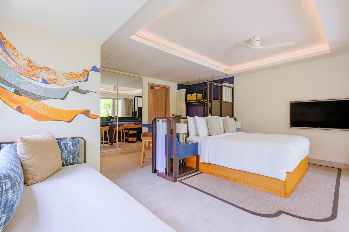 A modern hotel room with a large bed, a desk, a chair, and a TV.