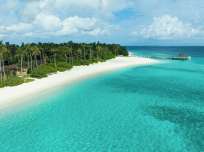A beach with a white sandy shore, clear turquoise water, and a pier extending into the sea. - Avani+ Fares Maldives Resort (Fares)