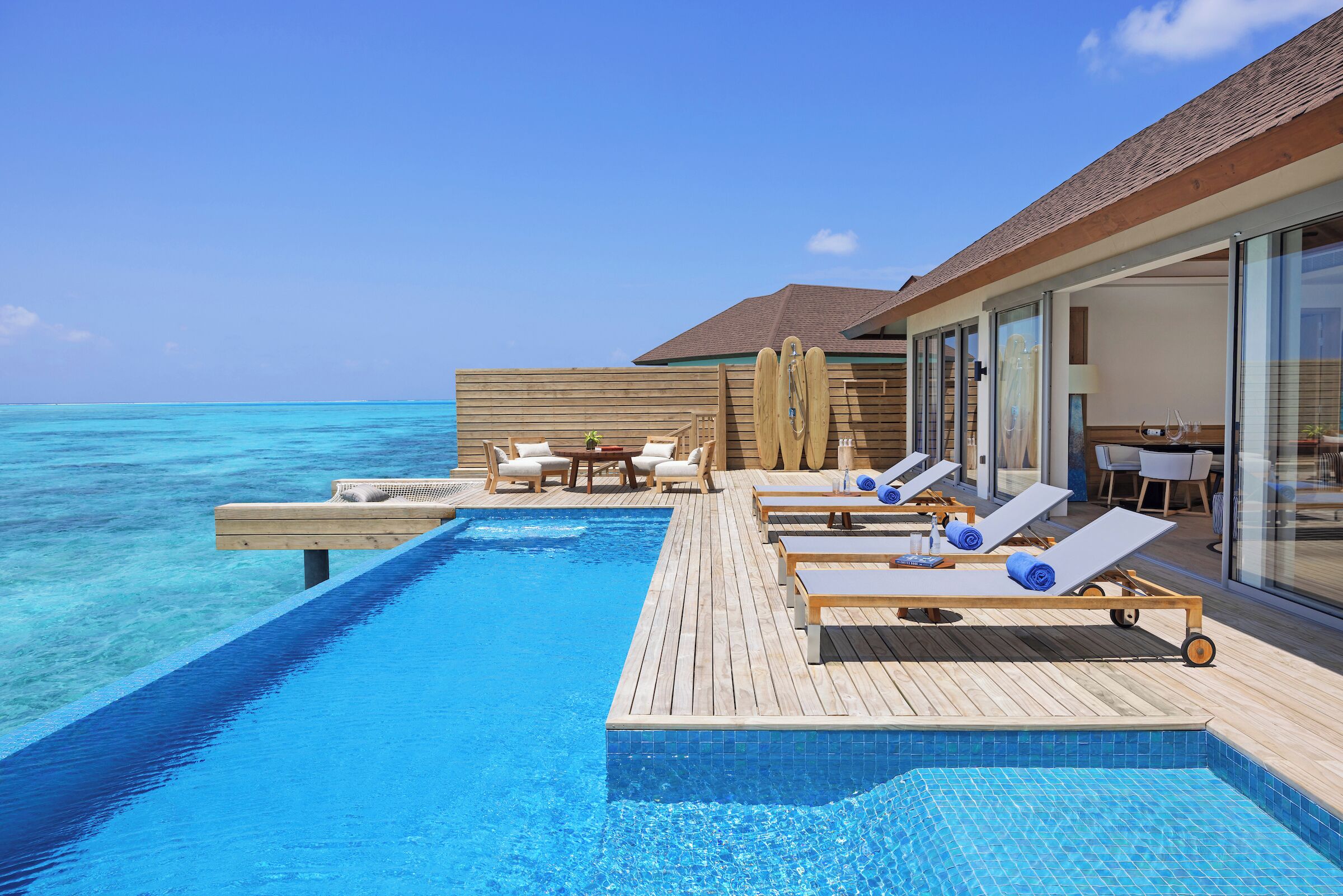 An infinity pool with lounge chairs and a wooden deck overlooking the ocean.