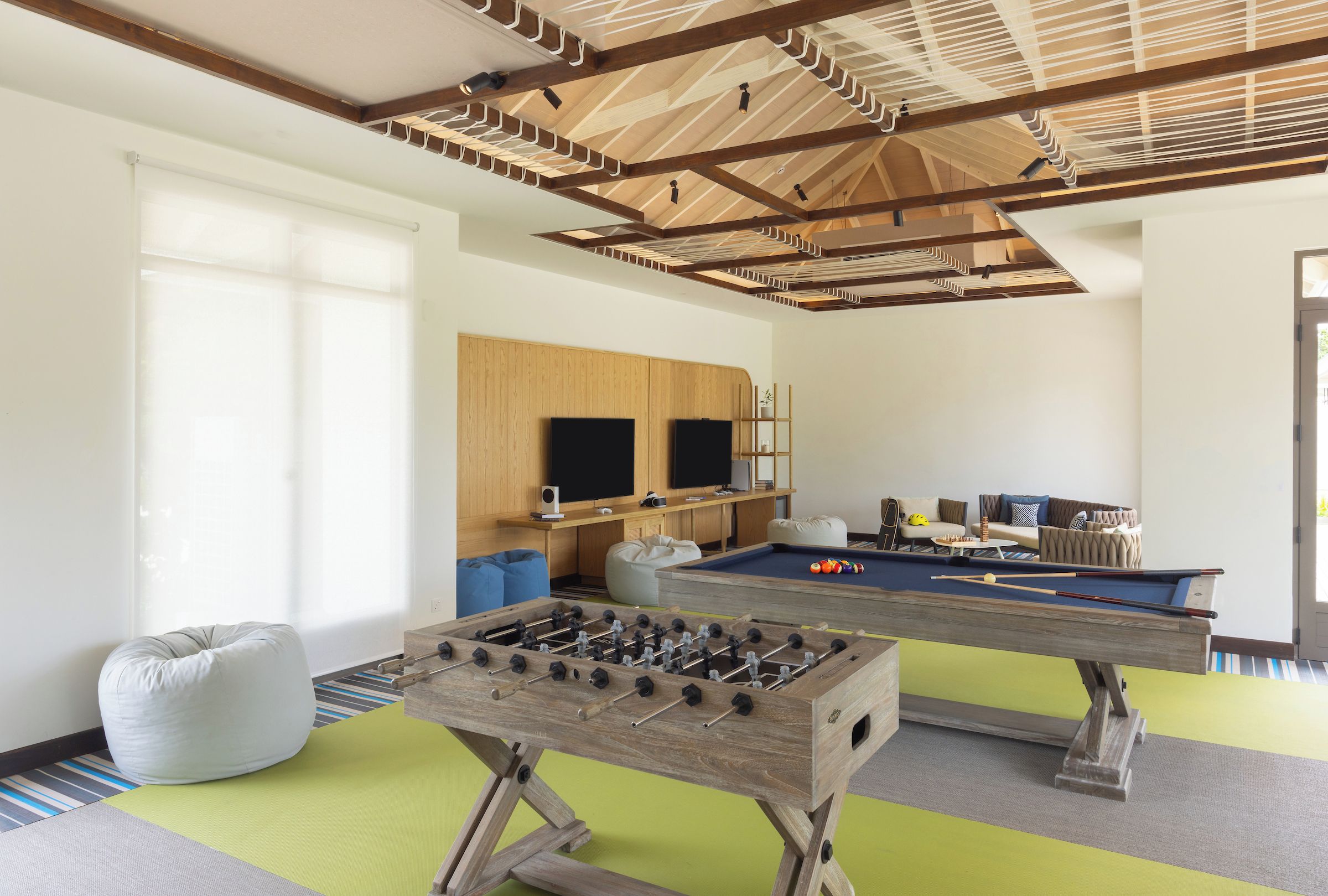 A room with a foosball table, a pool table, bean bags, and a television.