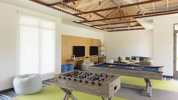 A room with a foosball table, a pool table, bean bags, and a television.