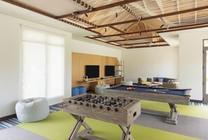 A room with a foosball table, a pool table, bean bags, and a television. - Avani+ Fares Maldives Resort (Fares)
