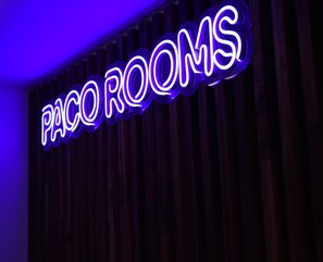 A neon sign with the text "PACCO ROOMS" against a dark background. - PACOROOMS (Madrid)