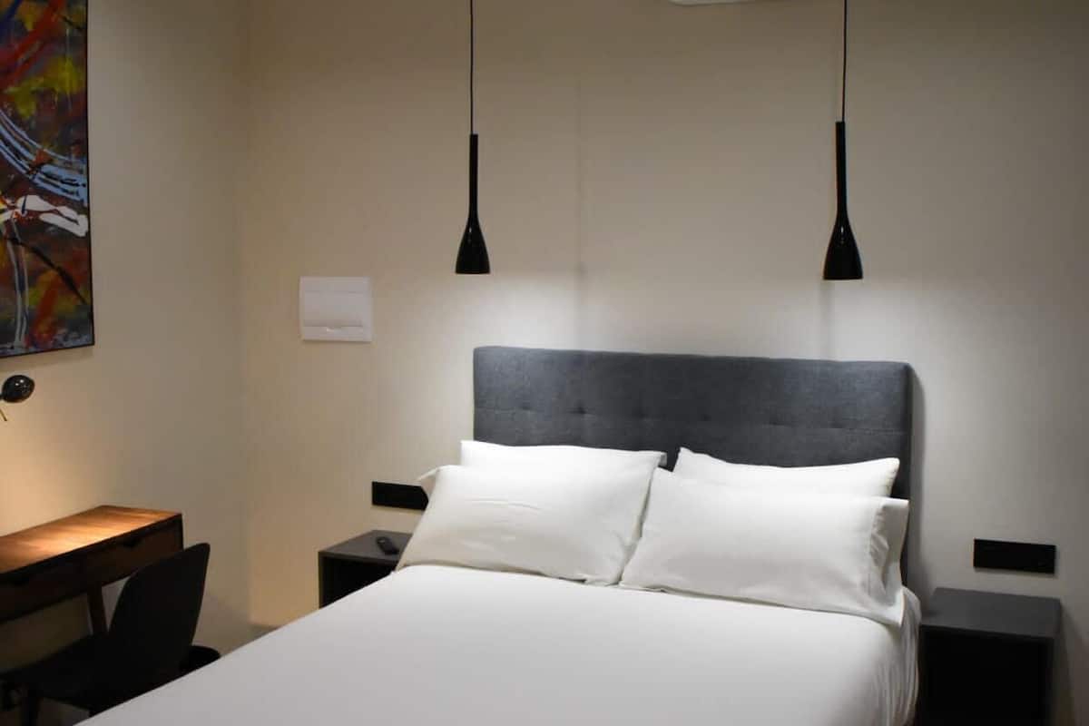 A bedroom with a bed, bedside tables, a desk, and an air conditioning unit.