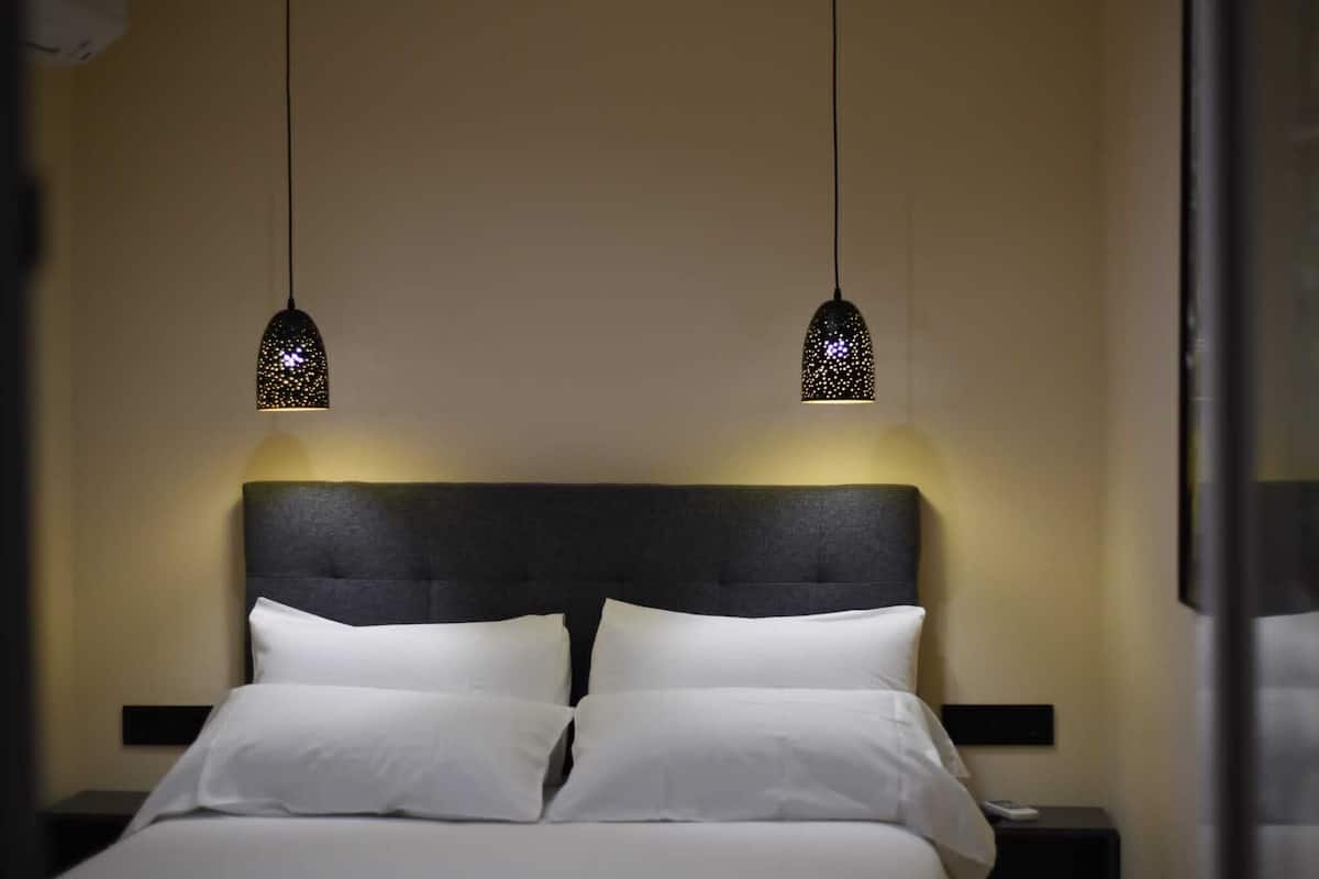 A hotel room with a neatly made bed, two pendant lights, and a dark headboard.