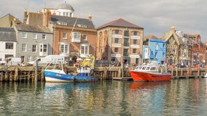 A waterfront with boats docked, buildings with signage, and a clear sky. - Cove Street Cottage (Weymouth)