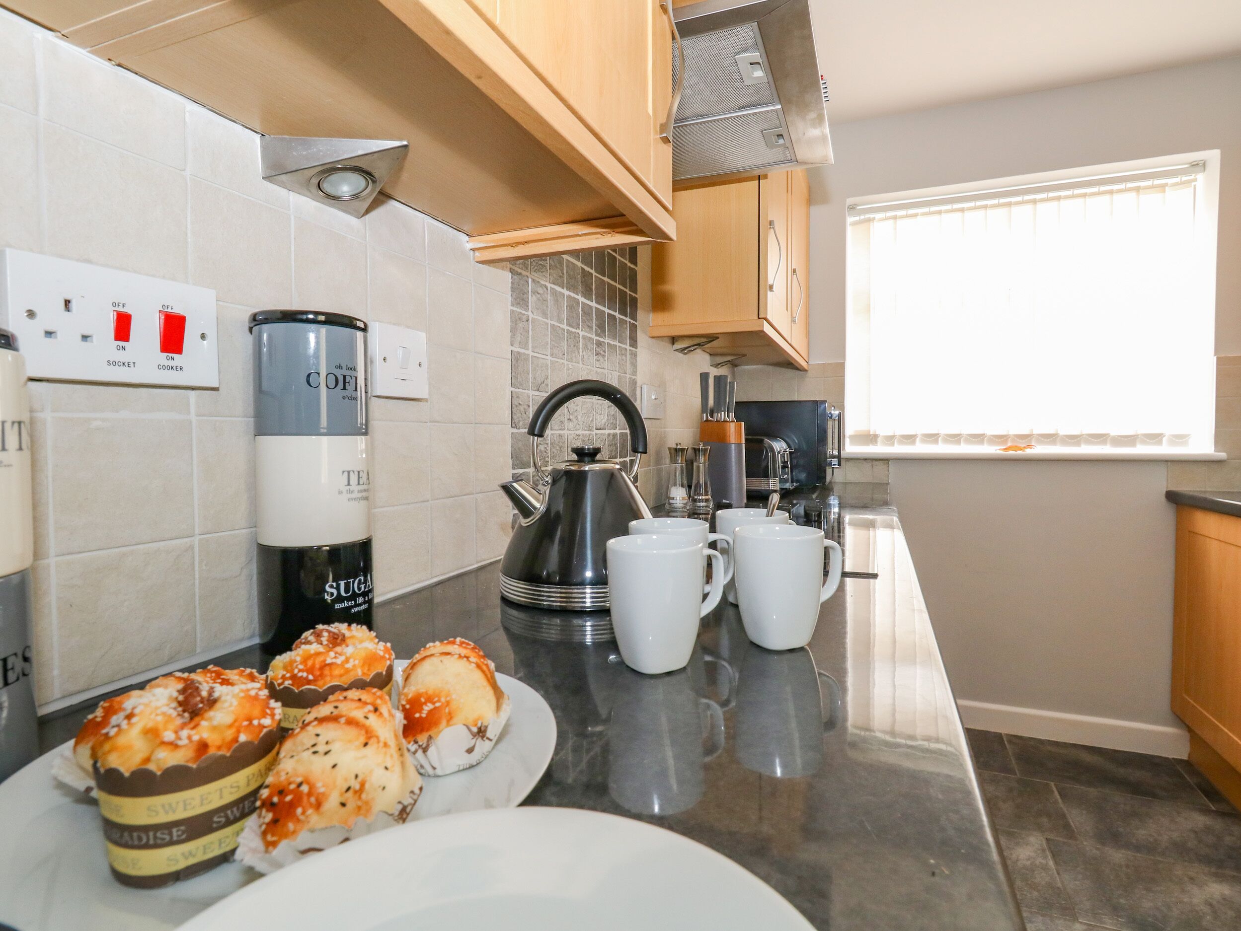 A kitchen with a coffee maker, kettle, and cups on the counter.