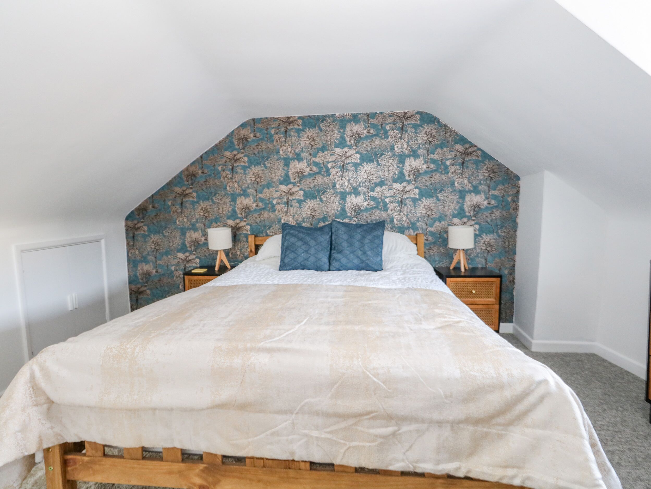 Un dormitorio con un cabecero estampado con motivos florales, un marco de cama de madera y dos mesitas de noche con lámparas.
