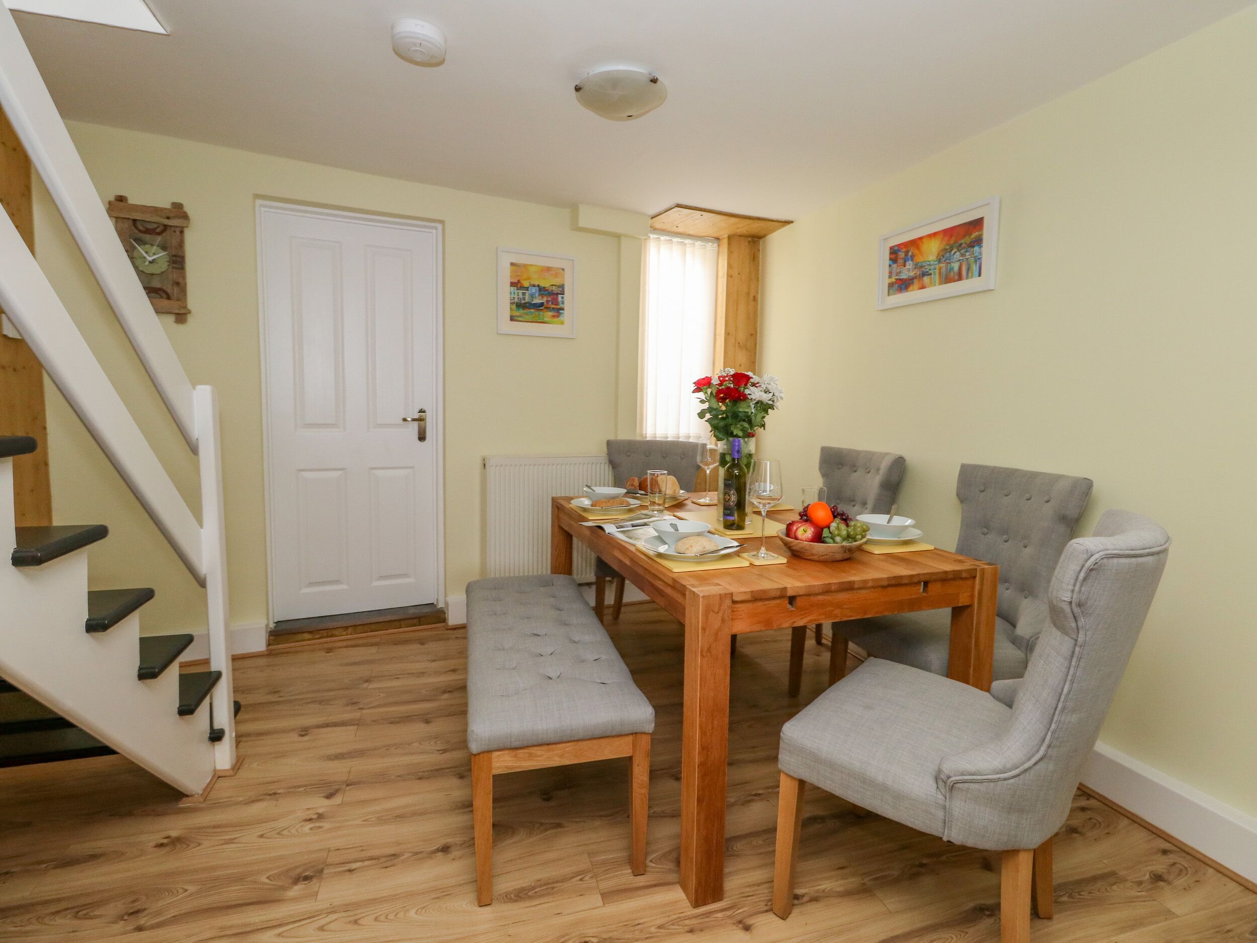 Un coin repas avec une table en bois, des chaises à revêtement gris, un vase avec des fleurs et un tableau accroché au mur.