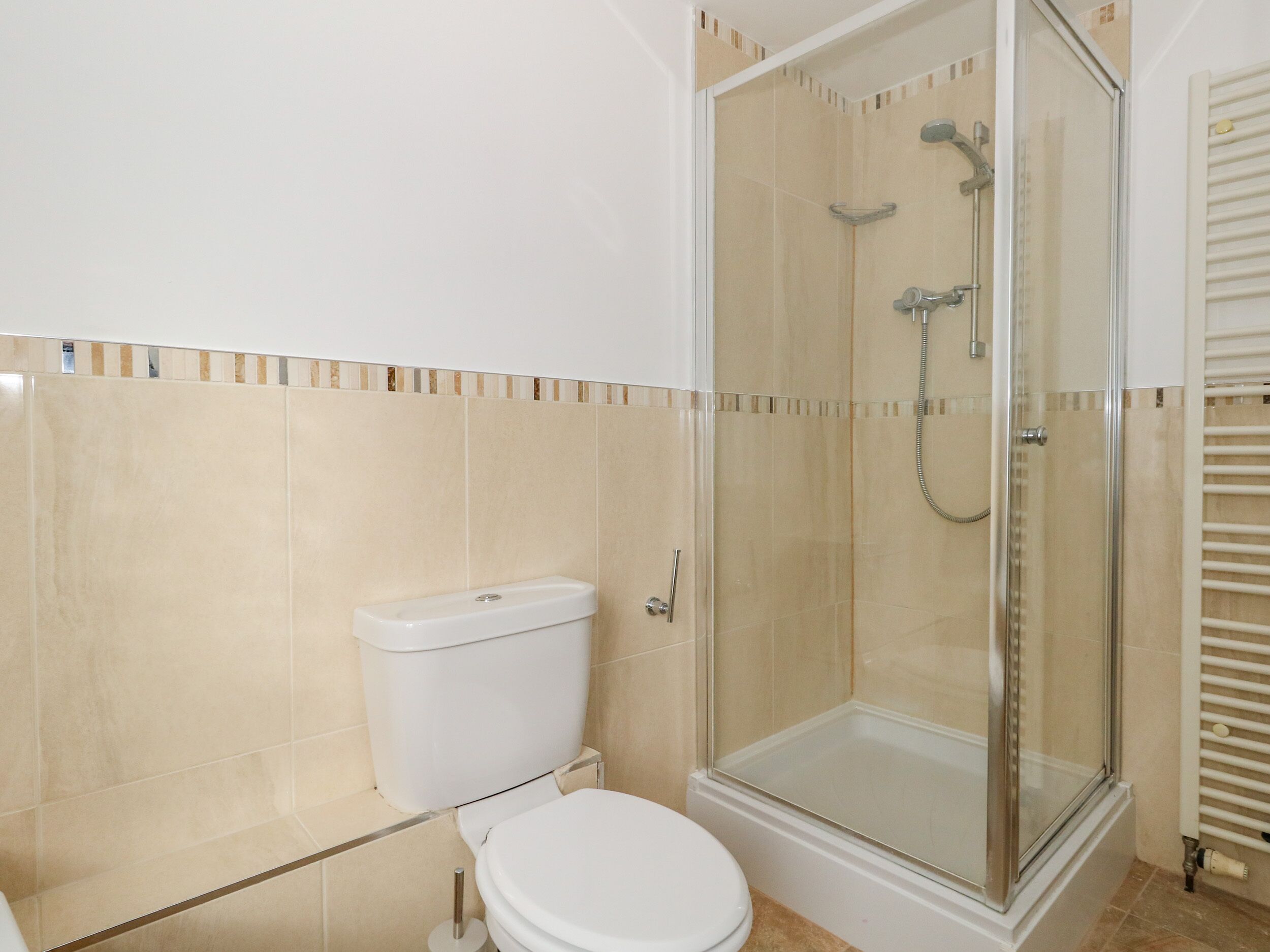 Une salle de bain comprenant des toilettes, une douche fermée par une paroi de verre et un mur recouvert de carreaux.