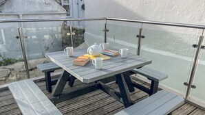 A wooden deck with a glass railing, a picnic table, and benches. - Cove Street Cottage (Weymouth)