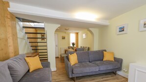 A living room with two grey sofas, wooden flooring, and a staircase leading to another room. - Cove Street Cottage (Weymouth)