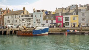 A waterfront with a blue and white boat docked at a pier, surrounded by colorful buildings. - Cove Street Cottage (Weymouth)