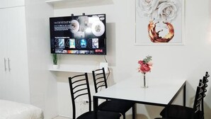 Un comedor moderno con una mesa blanca, sillas negras, un televisor montado en la pared y una decoración floral.