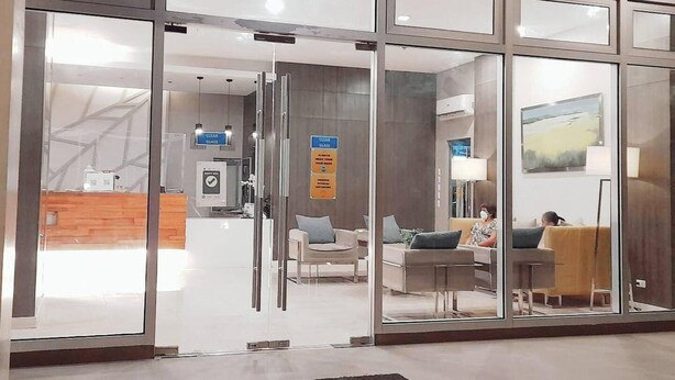 Un moderno vestíbulo de hotel con puertas de vidrio, un mostrador de recepción y una zona de estar con sofás y una mesa de centro.