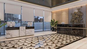 A modern reception area with marble countertops, a patterned floor, and large windows offering a view of the parking lot. - BeSS Mansion Hotel Surabaya (Wonocolo)