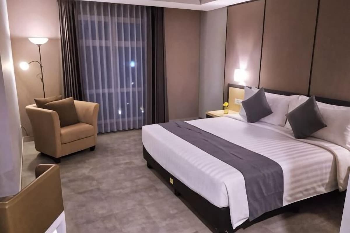 Une chambre d’hôtel avec un lit, une chaise, une table de chevet et une grande fenêtre avec des rideaux.