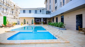A swimming pool with two lanes, surrounded by lounge chairs and potted plants, with a building in the background. - Exclusive Serene Hotel Abuja (Abuja)