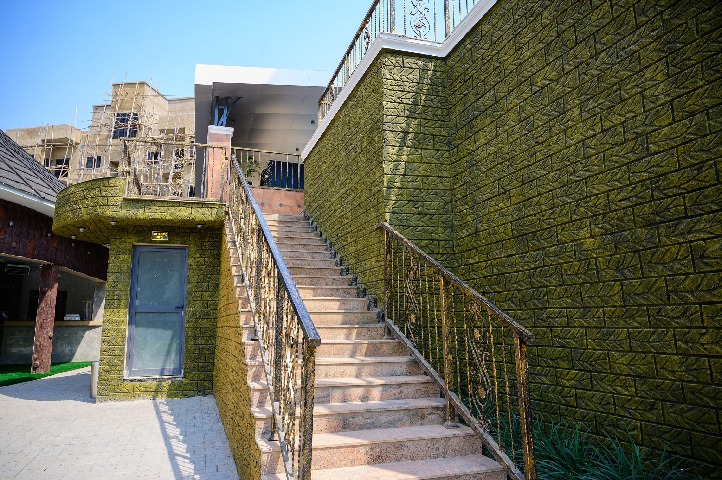 A staircase with a metal railing leading to a building with a textured green wall.