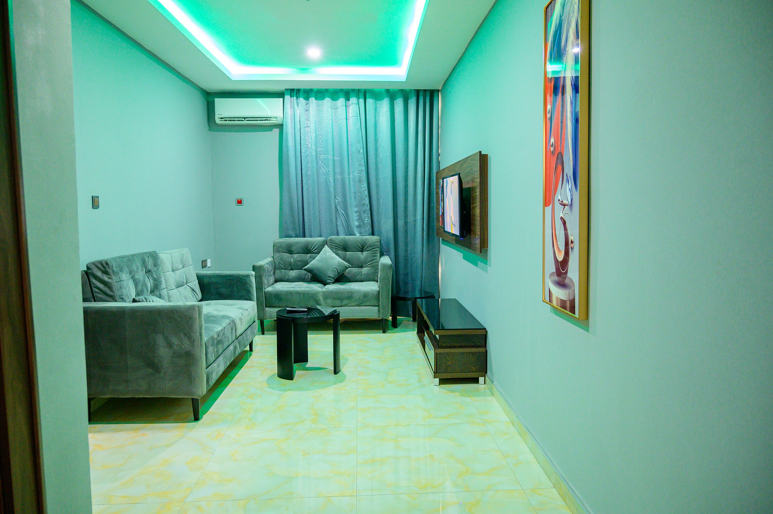 A living room with a grey sofa, a smaller grey armchair, a coffee table, and a TV mounted on the wall.