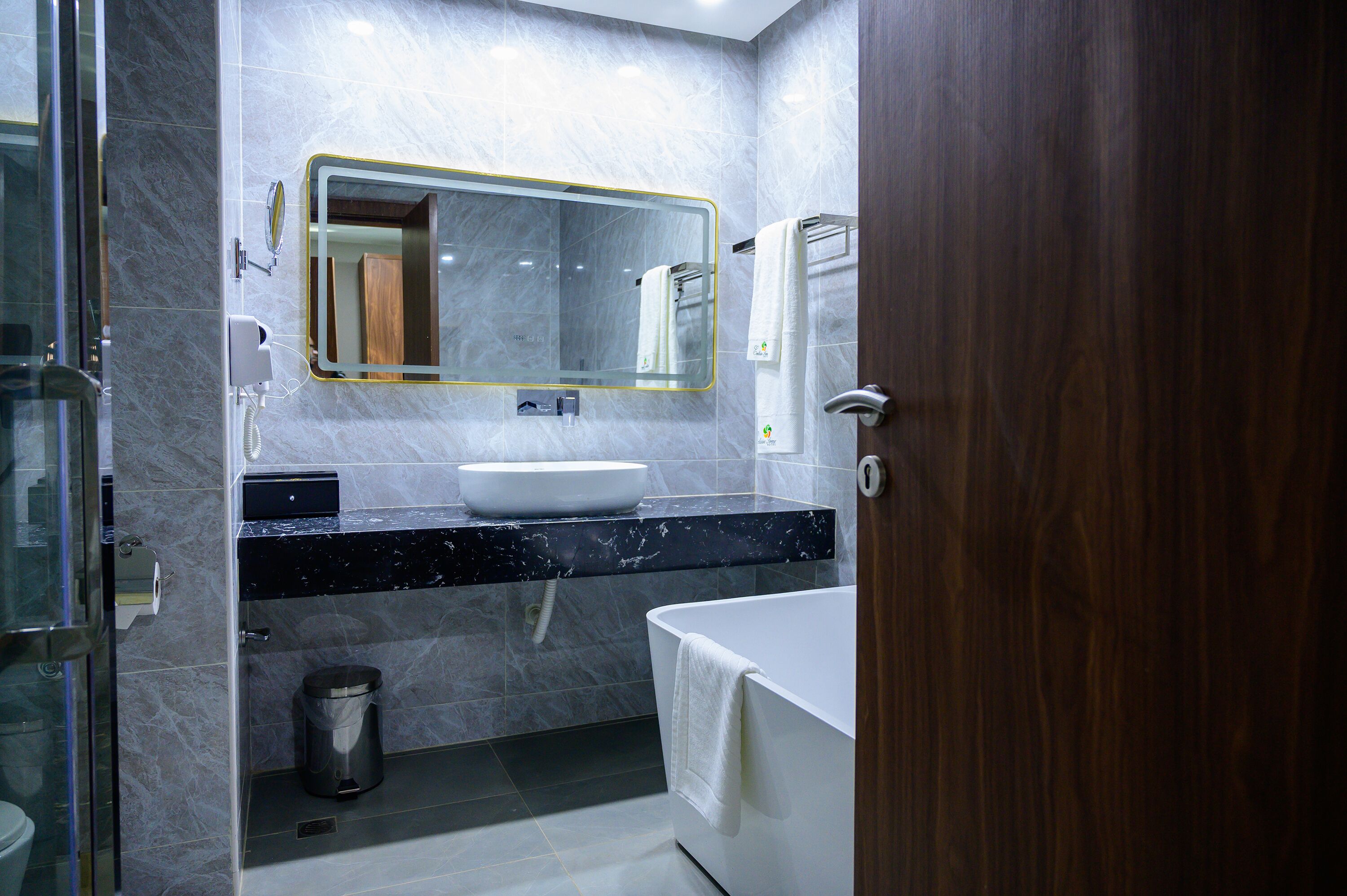 A modern bathroom with a marble sink, a large mirror, and a bathtub.