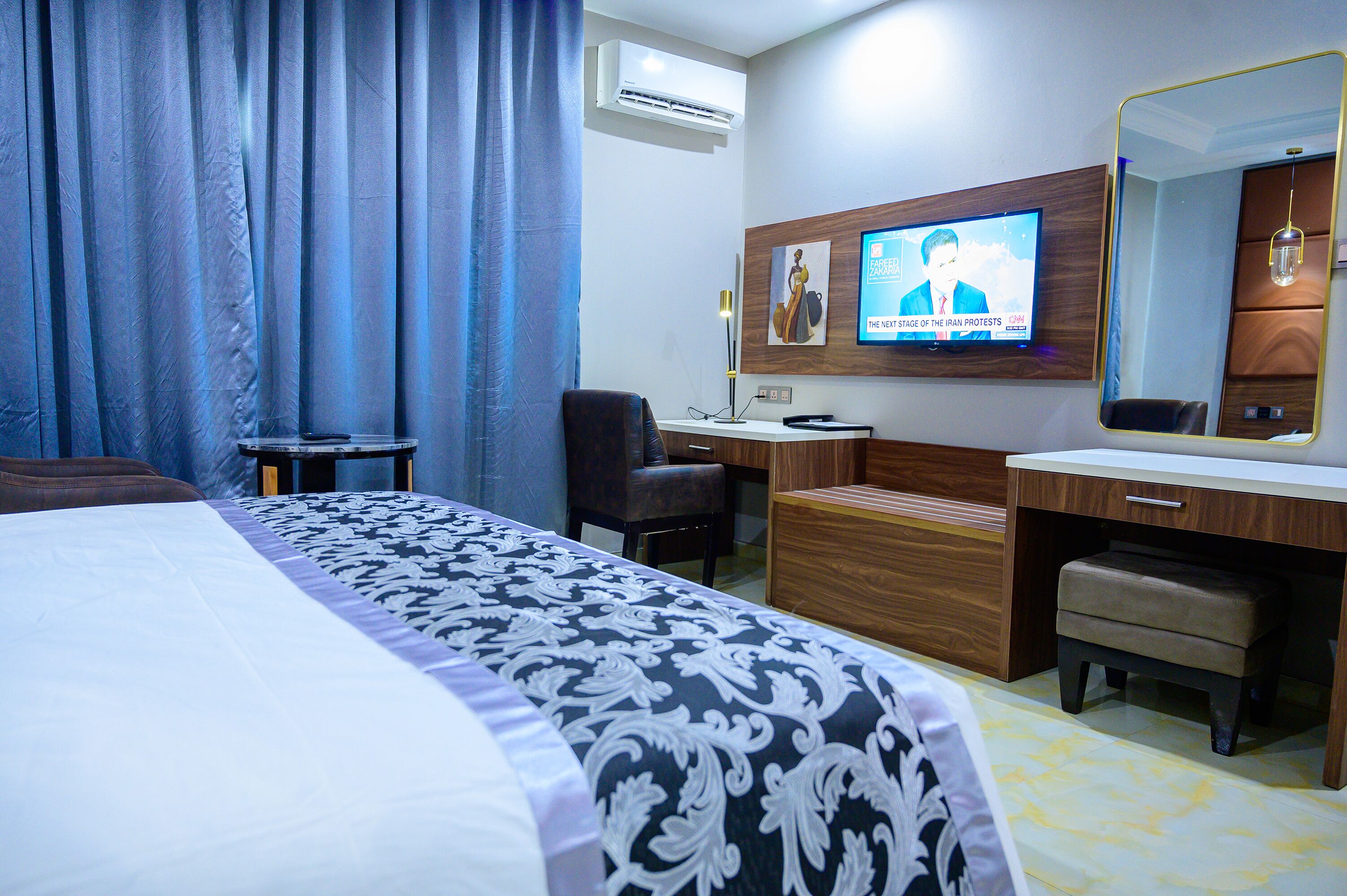 A hotel room with a bed, a desk, a chair, a television, and a mirror.