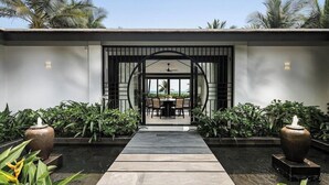 A modern entrance with a pathway leading to a dining area, surrounded by lush greenery and decorative vases. - TIA Wellness Resort (Da Nang Municipality)