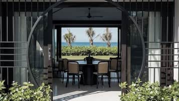 Uma área moderna para refeições ao ar livre com vista para o oceano, com um compartimento de vidro circular e um terraço com plantas em vasos.