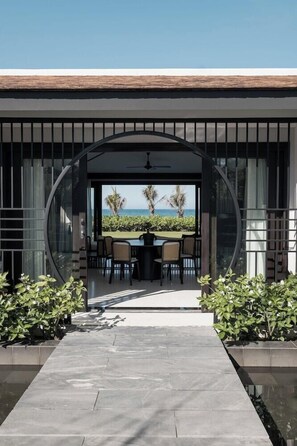 Uma área moderna para refeições ao ar livre com vista para o oceano, com um compartimento de vidro circular e um terraço com plantas em vasos.