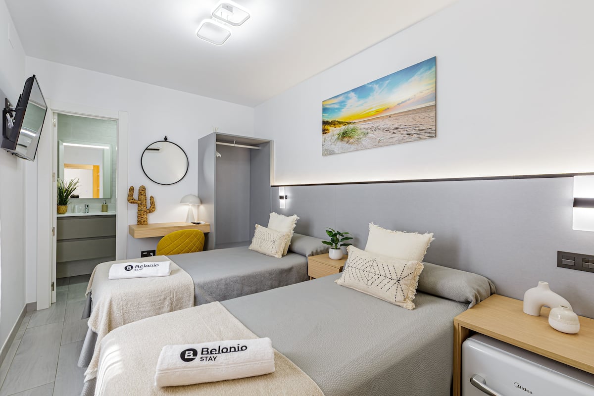 Ett hotellrum med två sängar, en platt-TV, en tavla som föreställer en strand och en minibar.
