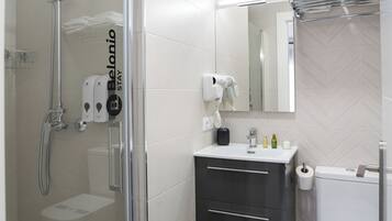 Un baño moderno con ducha de vidrio, tocador con espejo y retrete.