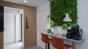 A modern kitchen with a wooden panel wall, a green plant wall, two pendant lights, a coffee machine, and two orange chairs. - Stay Belonio (Málaga)