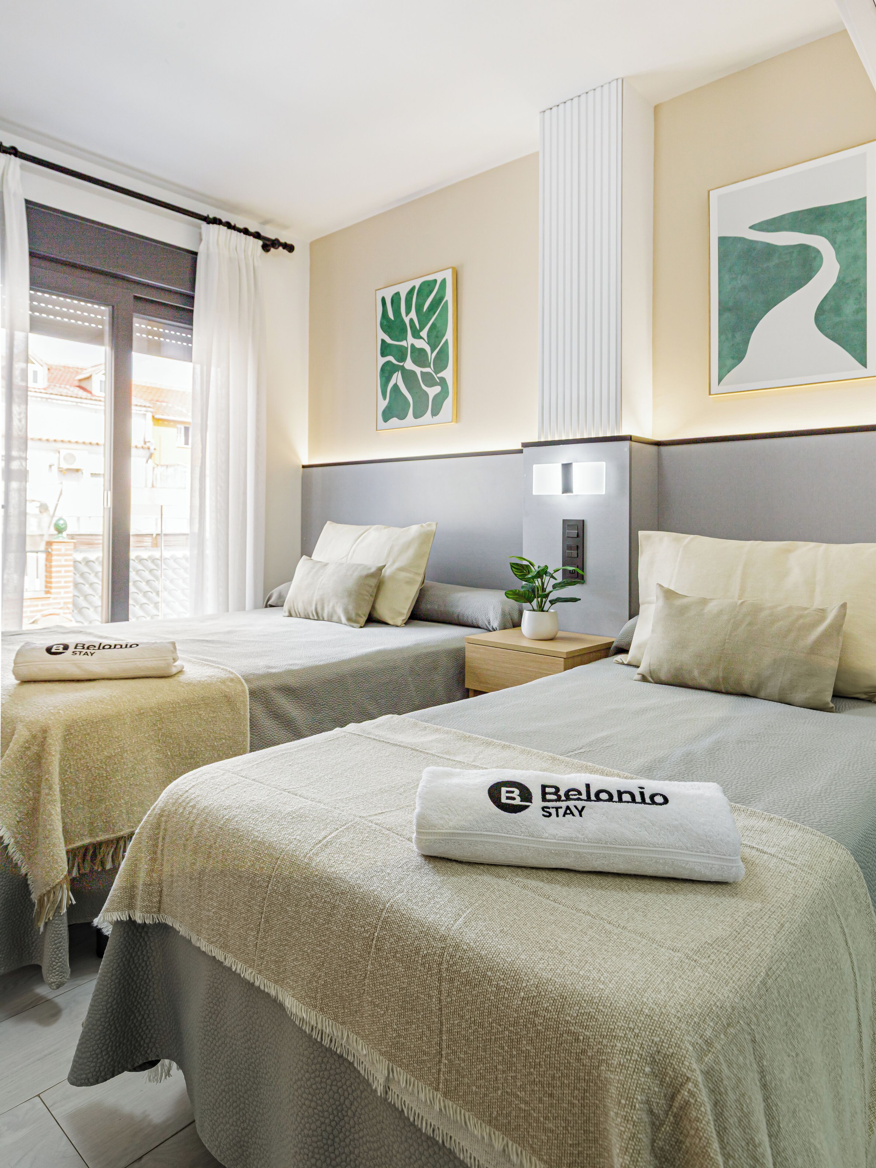 A hotel room with two beds, a small table with a plant, and a wall-mounted light.