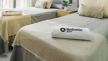 A hotel room with two beds, a small table with a plant, and a wall-mounted light.